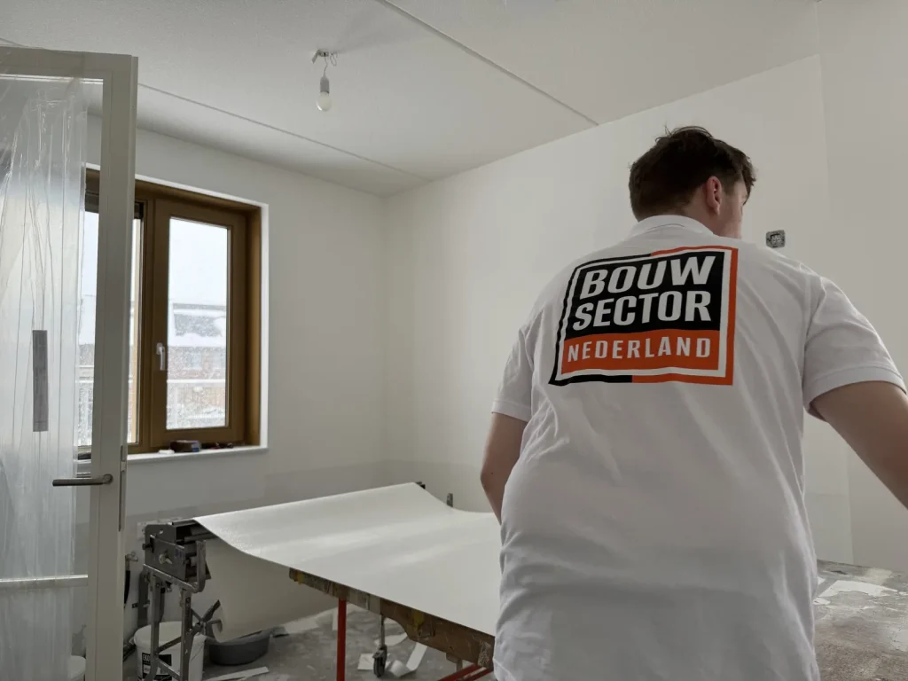 Vakman van Bouwsector Nederland bij de plaktafel met een baan vlies in een kamer met houten kozijn