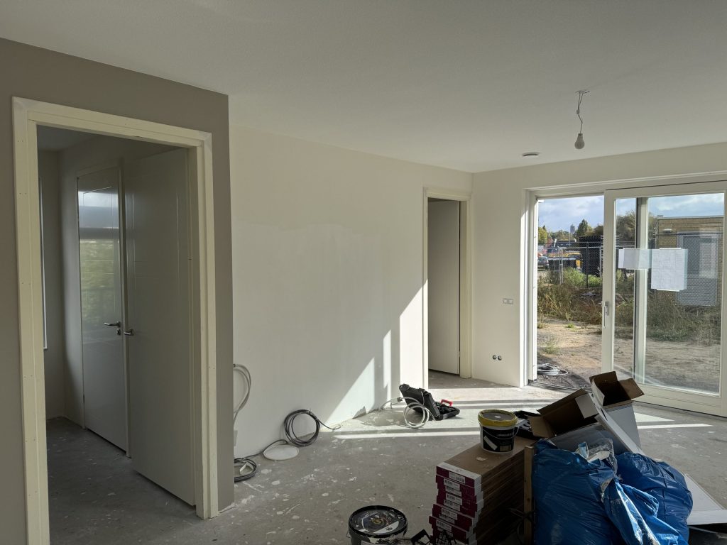 Nieuwe woonkamer in afwerking met kale wanden, openstaande deuren en materiaal op de betonvloer