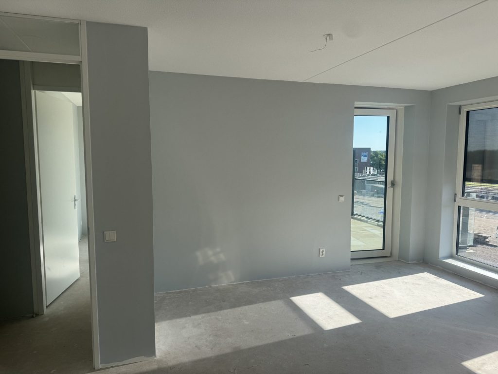 Appartement met lichtgrijze wanden, een balkondeur en een kale betonvloer