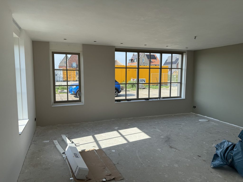 Woonkamer met warme grijze wanden en grote raampartijen in een nieuwbouwwoning