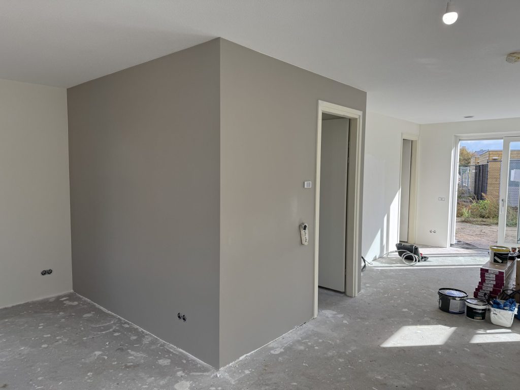 Grijs afgewerkte wand rond de meterkast in een nieuwe woning, met verfemmers op de vloer