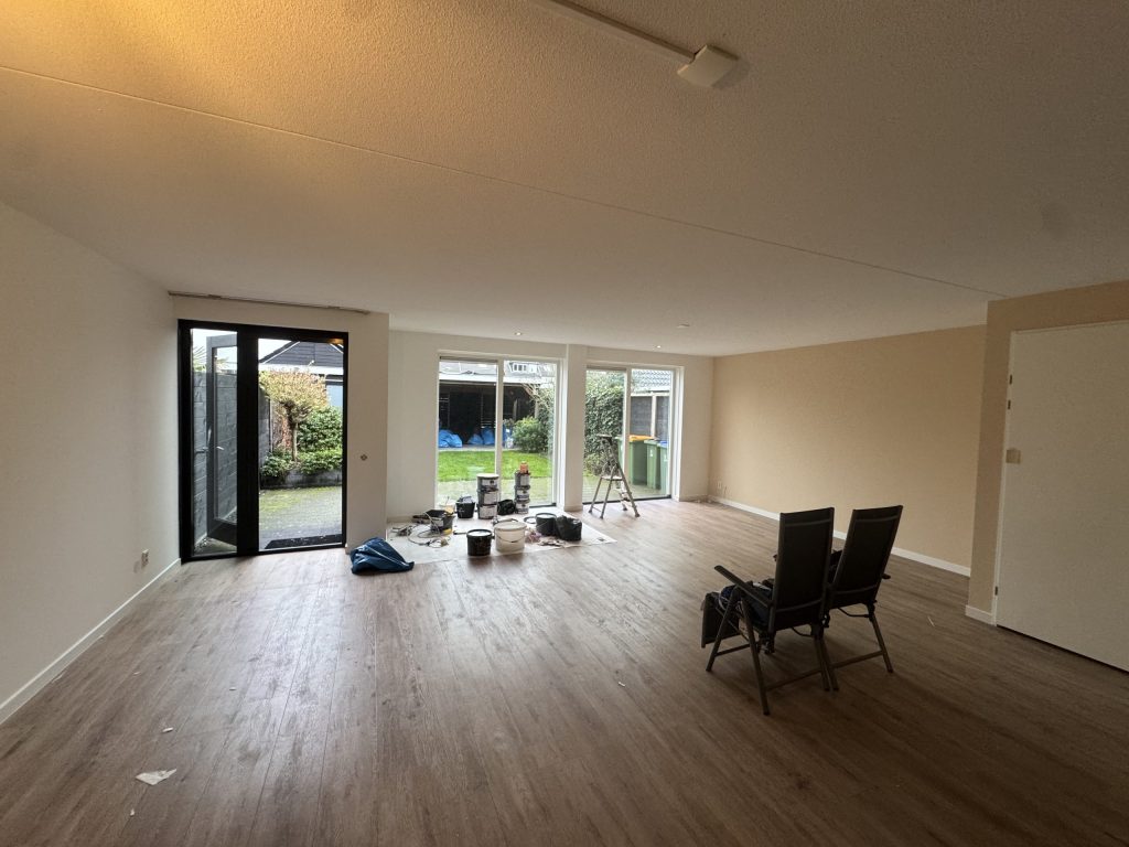 Lege woonkamer met lichte, strak afgewerkte wanden, een houten vloer en drie tuindeuren