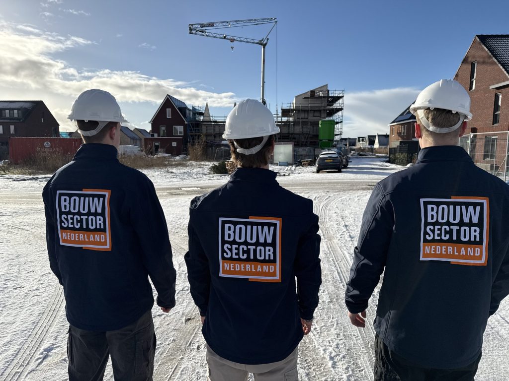 Drie vakmensen van Bouwsector Nederland met witte helm voor huizen in aanbouw en een bouwkraan